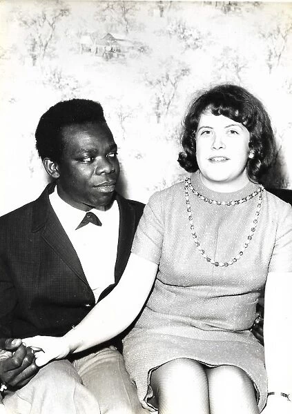 Black man and white woman sitting on a bed holding hands