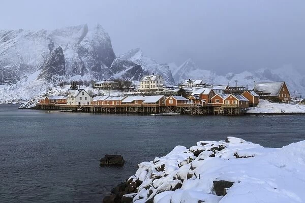 Snowy peaks and rorbu, the red houses of fishermen, in the landscape of the Lofoten Islands, Arctic, Norway, Scandinavia, Europe