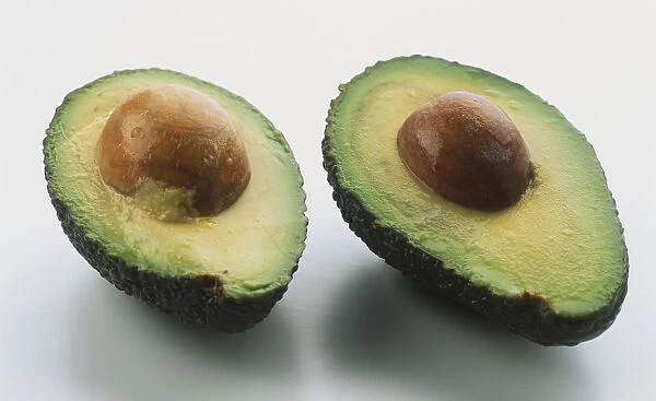 Two avocado halves, stone left in both, close up