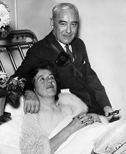 Authoress Enid Blyton in hospital lying in bed comforted by her husband Kenneth Darrell