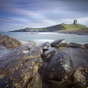 Dunstanburgh Castle bathed in afternoon sunlight with rocky coastline in foreground
