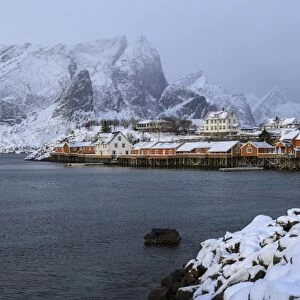 Snowy peaks and rorbu, the red houses of fishermen, in the landscape of the Lofoten Islands, Arctic, Norway, Scandinavia, Europe