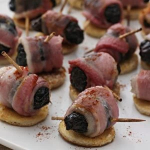Devils On Horseback, prunes stuffed with mango chutney and wrapped in bacon, sprinkled with cayenne pepper, arranged on toasted slices of bread, close-up
