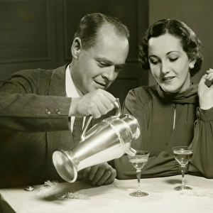 Couple sitting at table, man pouring drinks, (B&W)