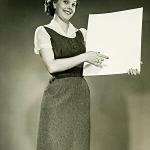Woman holding blank sheet of paper, posing in studio, (B&W), portrait