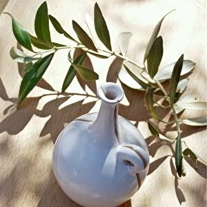Ceramic oil bottle on tabled dappled in Italian sunshine with branch from olive tree