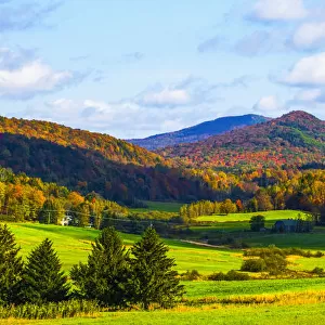 Landscape of forests on the hills with autumn coloured foliage and lush green fields
