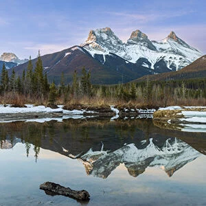 Three Sisters snow-capped mountain peaks reflected in a mirror image in a lake in Alberta, Canada; Canmore, Alberta, Canada