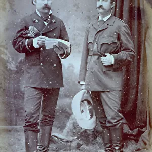 Full-length portrait of two soldeirs, one in uniform and the other in travel dress. The man in uniform holds a book, the other one a hat